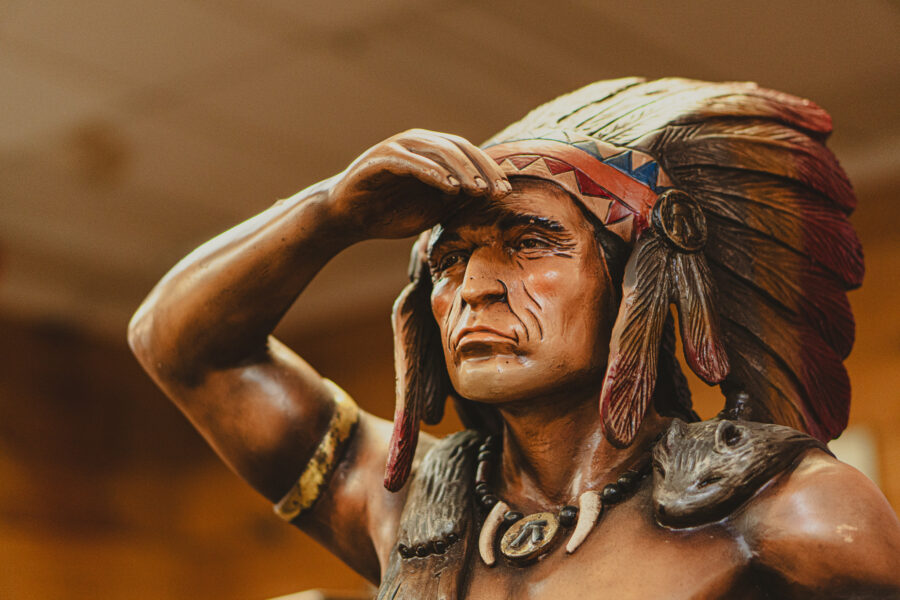 Hand-carved wooden Native American chief statue with feather headdress, available at Castle Antiques Haliburton Ontario.