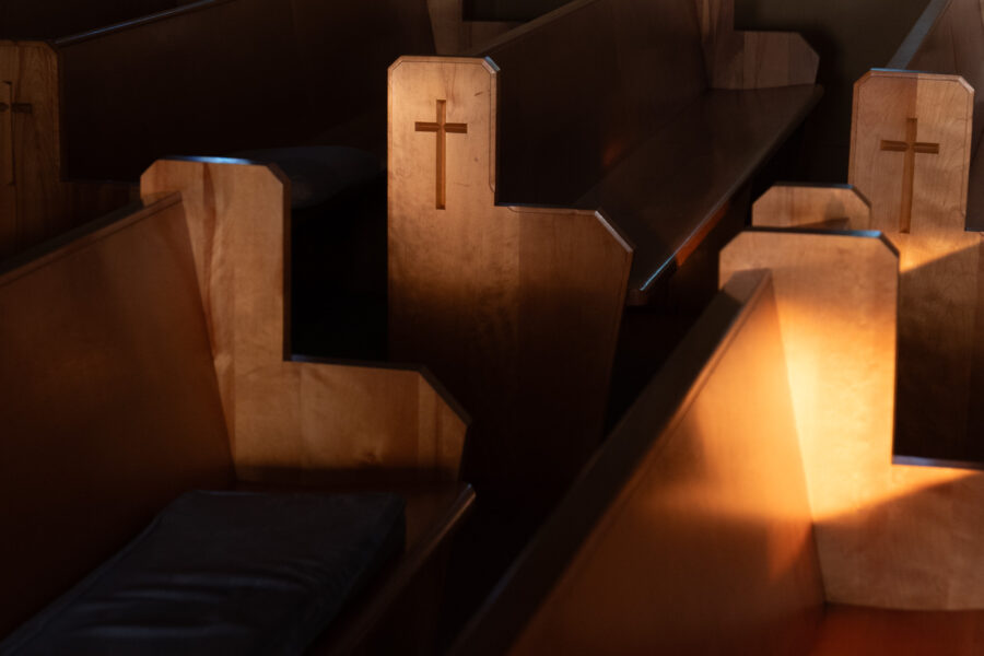 Wooden church pews with carved crosses, illuminated by warm sunlight, at Our Lady of Fatima Church, Minden, Ontario