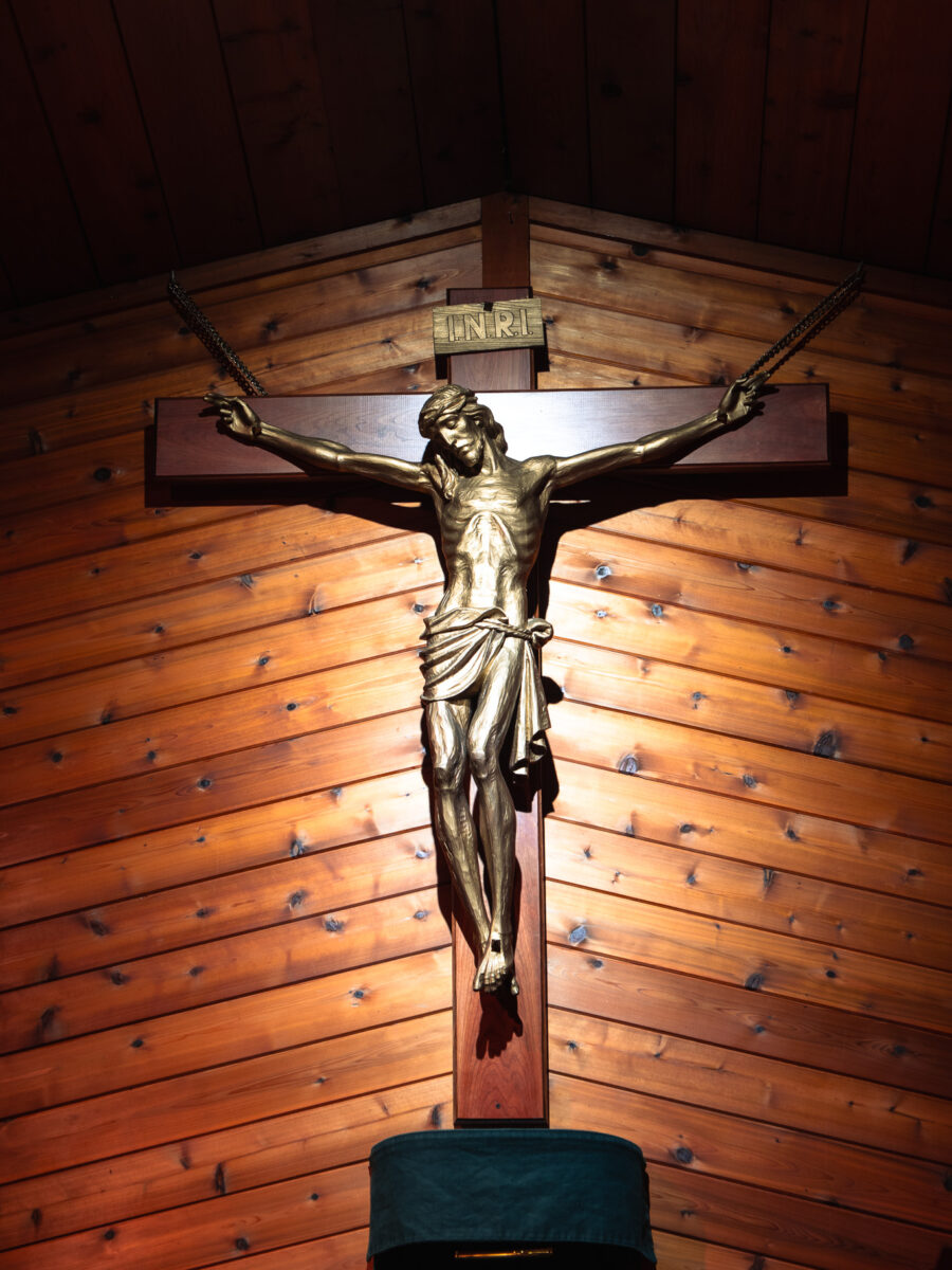 Large wooden crucifix with gold-toned corpus of Jesus Christ against a wood-paneled wall at Our Lady of Fatima Church, Minden, Ontario.