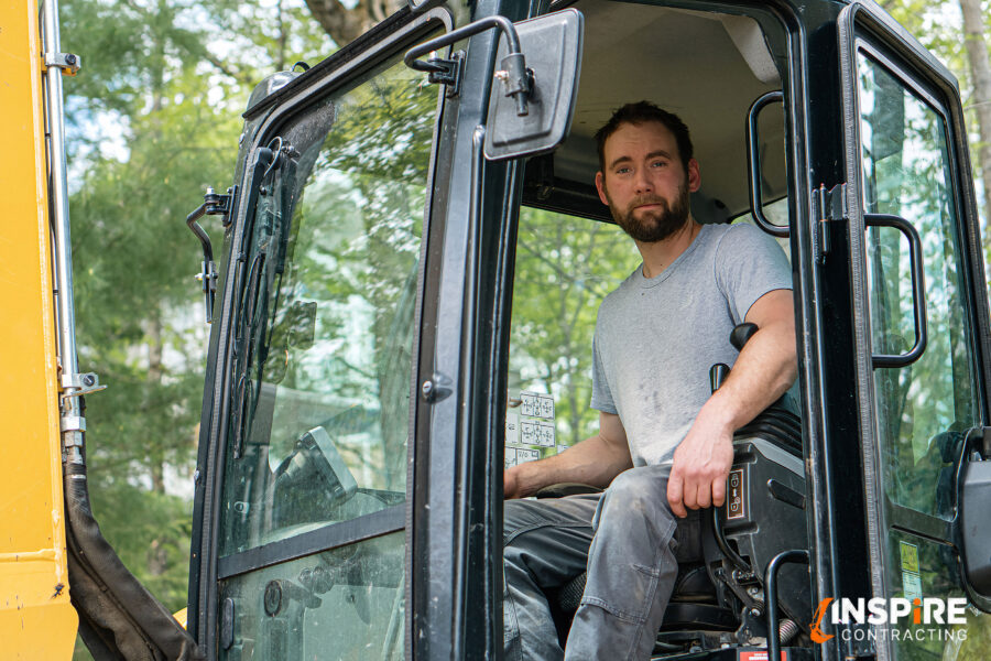 Tyler Hall guiding excavator bucket placement during septic system installation in Haliburton